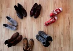 6 Schuhpaare ordentlich im Kreis aufgestellt, ein Paar roter Chucks verlassen den Kreis