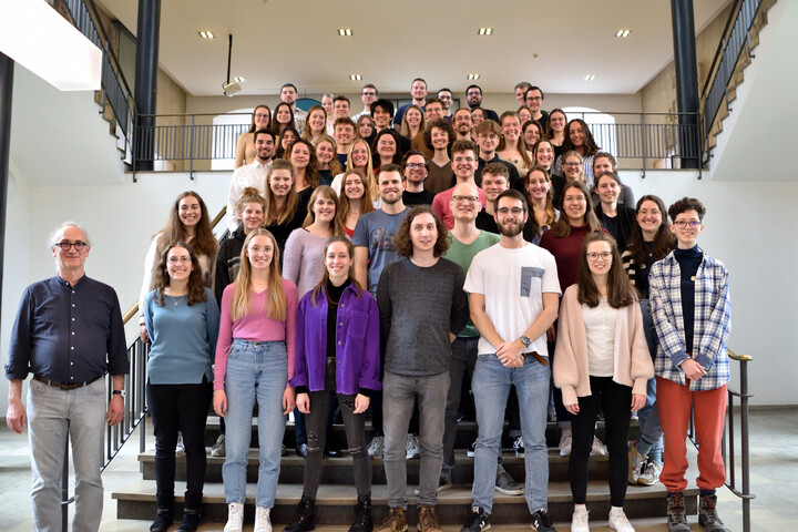 Eine Gruppe junger Studierenden steht bunt gekleidet auf einer Treppe.