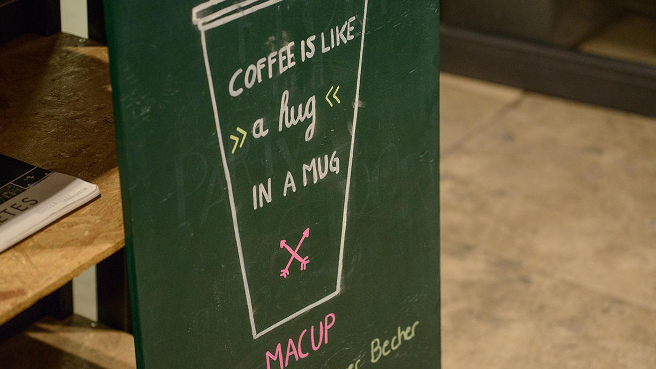 Eine dunkelgrüne Kreidetafel mit der weißen Aufschrift "Coffee is like a hug in a mug".