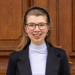 Jolina Sieland. Jolina trägt Brille, einen Haarreif und einen schwarzen Blazer. Sie lächelt freundlich in die Kamera.