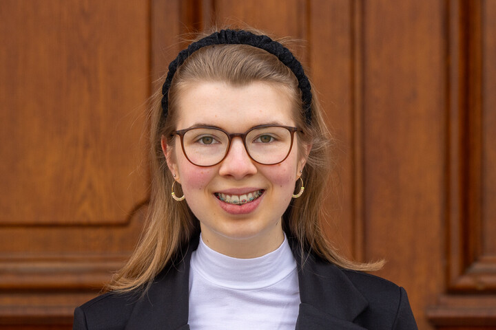 Jolina Sieland. Jolina trägt Brille, einen Haarreif und einen schwarzen Blazer. Sie lächelt freundlich in die Kamera.