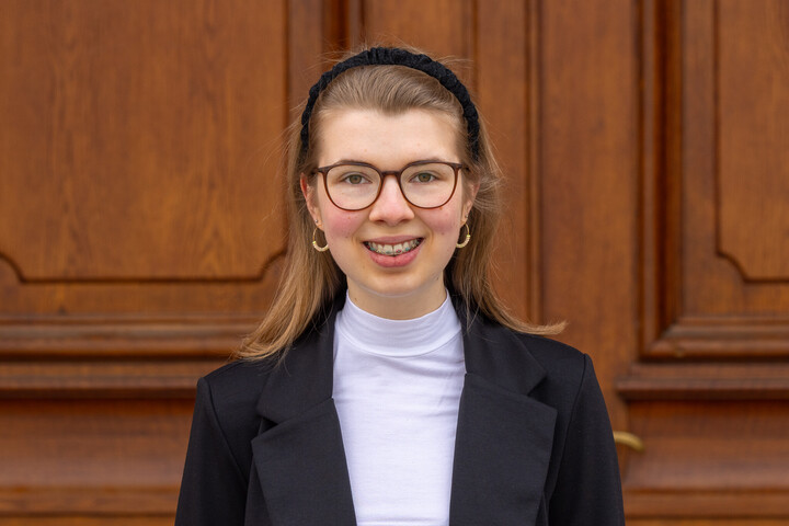 Jolina Sieland. Jolina trägt Brille, einen Haarreif und einen schwarzen Blazer. Sie lächelt freundlich in die Kamera.