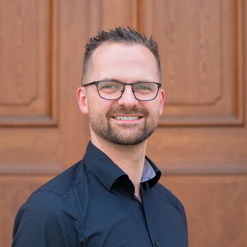 Lukas Dausend hat kurze braune Haare und einen Bart. Er trägt eine Brille und ein schwarzes Hemd.