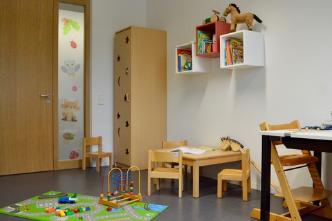 Eltern-Kind-Zimmer der Universität Mannheim. Auf dem Boden liegt ein Teppich mit Spielsachen darauf und daneben ist ein kleiner Tisch mit kleinen Stühlen.