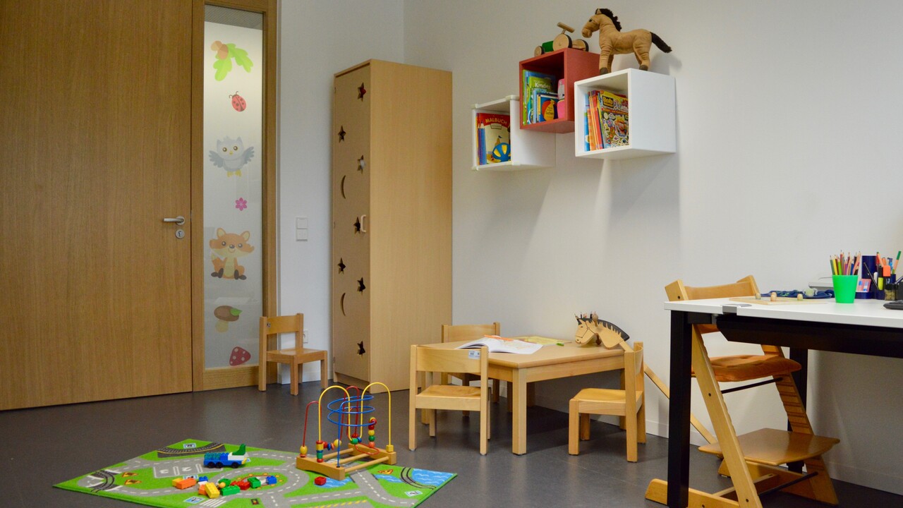Eltern-Kind-Zimmer der Universität Mannheim. Auf dem Boden liegt ein Teppich mit Spielsachen darauf und daneben ist ein kleiner Tisch mit kleinen Stühlen.