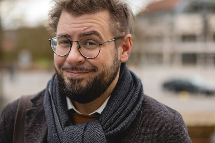Hiram Kümper. Hiram Kümper trägt Brille, einen blauen Schal und ein schwarzes Sakko. Über seiner Schulter hängt eine braune Tasche.