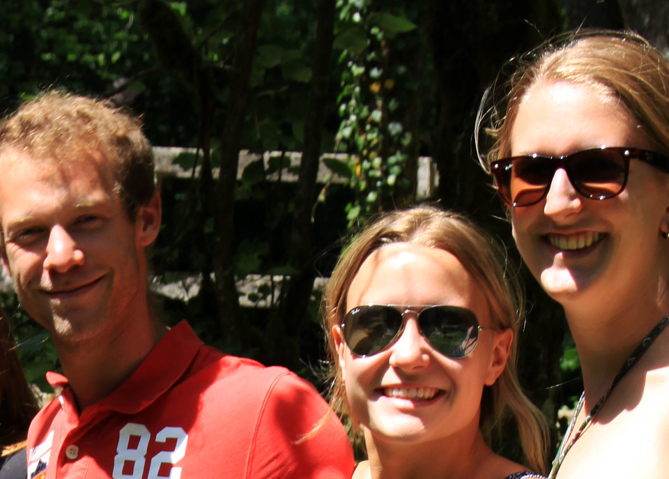 Zwei blonde Frauen mit Sonnenbrille und ein blonder Mann in rotem Poloshirt stehen zusammen und lachen in die Kamera.