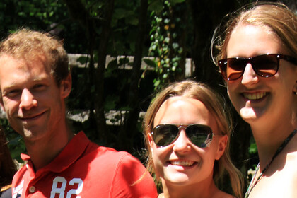 Zwei blonde Frauen mit Sonnenbrille und ein blonder Mann in rotem Poloshirt stehen zusammen und lachen in die Kamera.