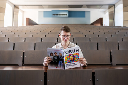 Ein Student sitzt in der Mitte eines leeren Hörsaals und liest im FORUM 1/2026.