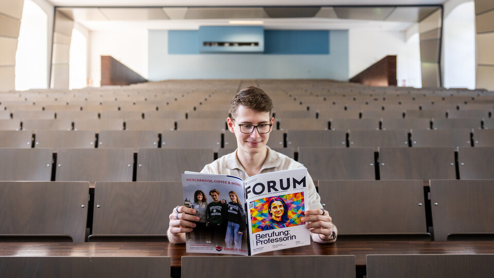 Ein Student sitzt in der Mitte eines leeren Hörsaals und liest im FORUM 1/2026.