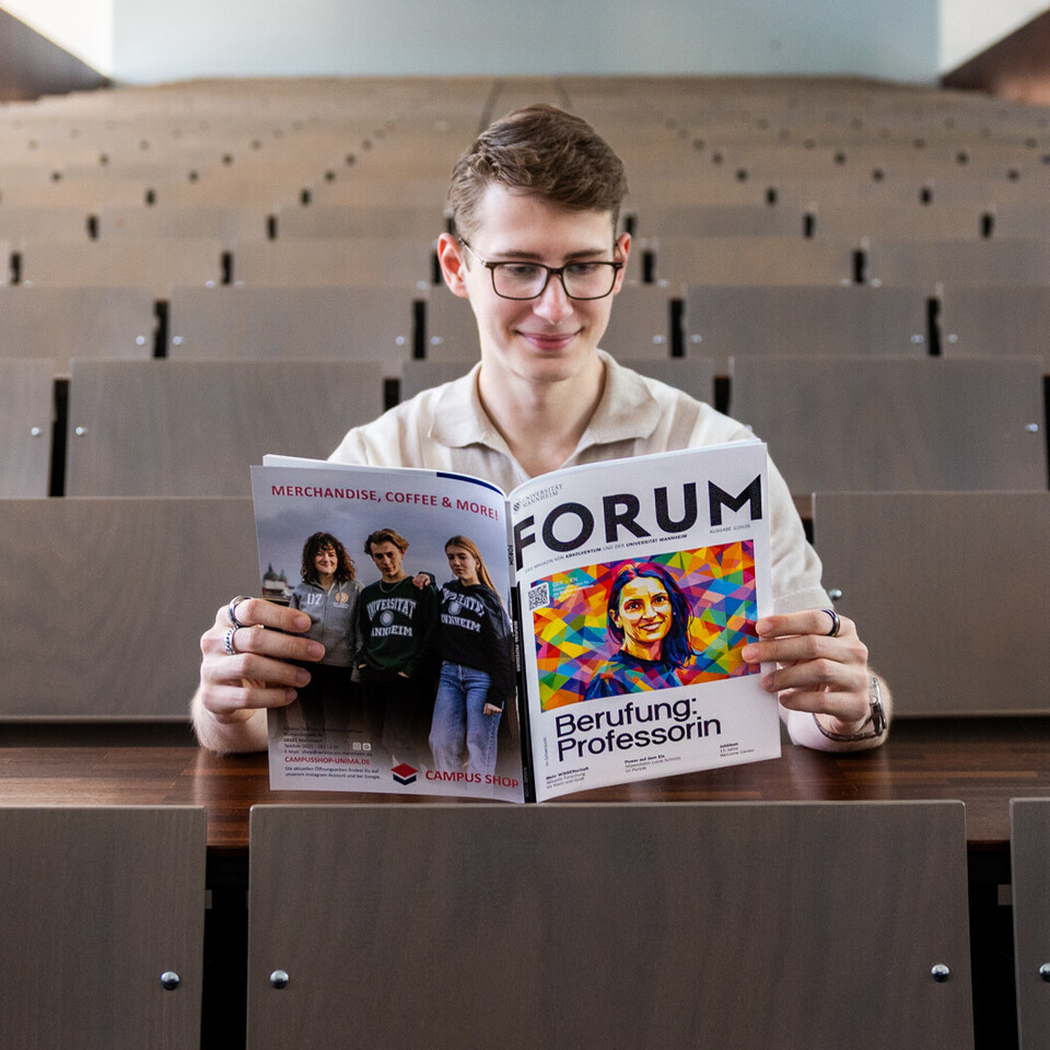 Ein Student sitzt in der Mitte eines leeren Hörsaals und liest im FORUM 1/2026.