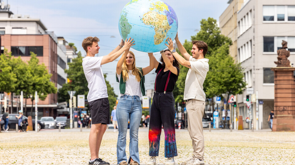 Vier Studierende stehen auf dem Ehrenhof und halten eine aufgeblasene Weltkugel in die Höhe. Im Hintergrund sind Gebäude aus der Stadt zu sehen.