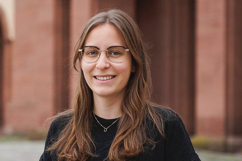 Marlene Fritz hat braune lange Haare. Sie trägt eine goldumrandete Brille und ein schwarzes T-Shirt.