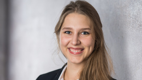 Fabienne Partsch. She is wearing a black jacket and is standing next to a grey wall.