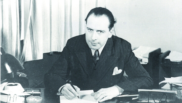 Eine schwarzweiß Fotografie. Paul Eppstein sitzt im Anzug an einem Schreibtisch und schreibt mit einem Stift in einem Büchlein.