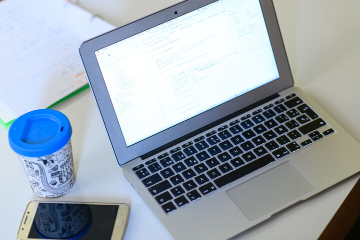 Aufgeklapptes Laptop, neben dem ein Kaffee steht und ein Smartphone liegt.