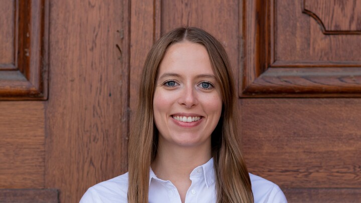 Emilia Gschoßmann. She is wearing a white shirt and is standing in front of one of the castle doors.
