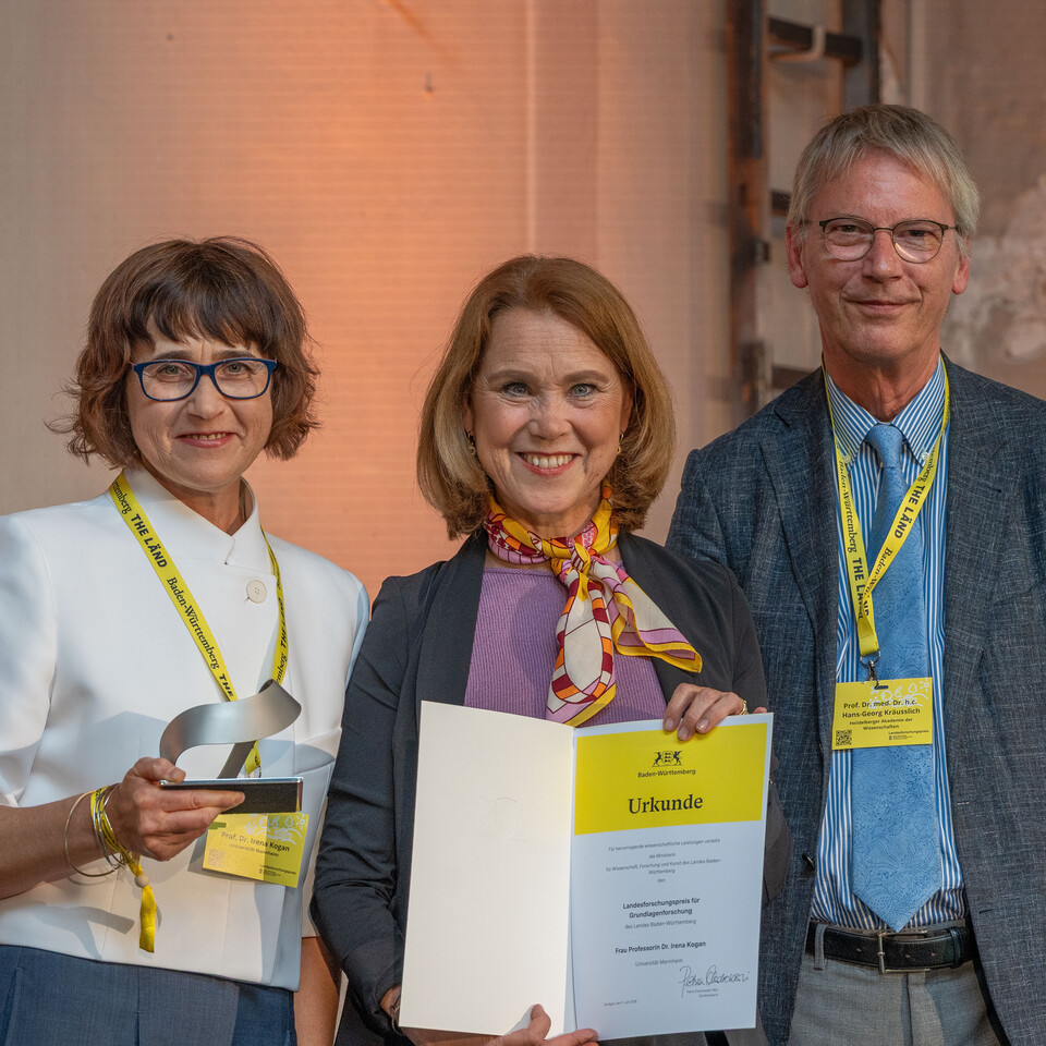 Professorin Kogan steht mit Ministerin Olschowski und mit Hans-Georg Kräusslich auf der Bühne und hält ihre Auszeichnung in der Hand.