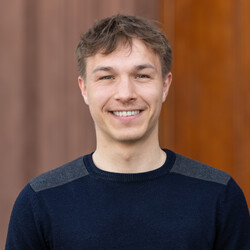 Johannes lächelt freundlich in die Kamera. Er trägt einen dunklen Pullover. 