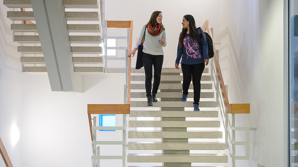 Zwei Studentinnen unterhalten sich und laufen die Treppe im Gebäude L 1 runter.