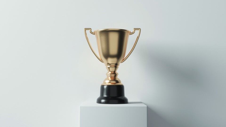 Goldener Pokal auf einem weißen Sockel vor einer weißen Wand.