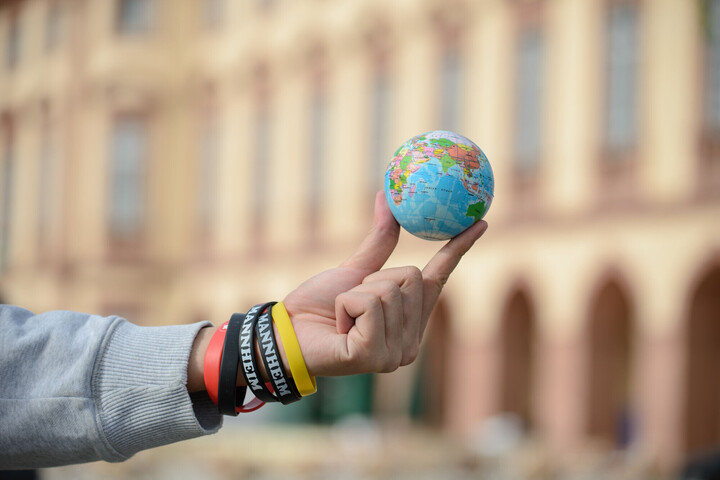 Eine Hand hält einen kleinen Weltkugelball mit zwei Fingern in die Luft.