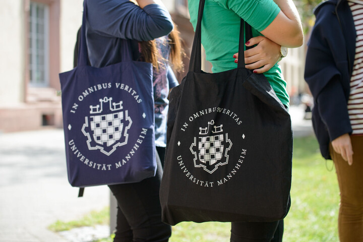Zwei Studierende mit Universität Mannheim Taschen laufen über den Campus.