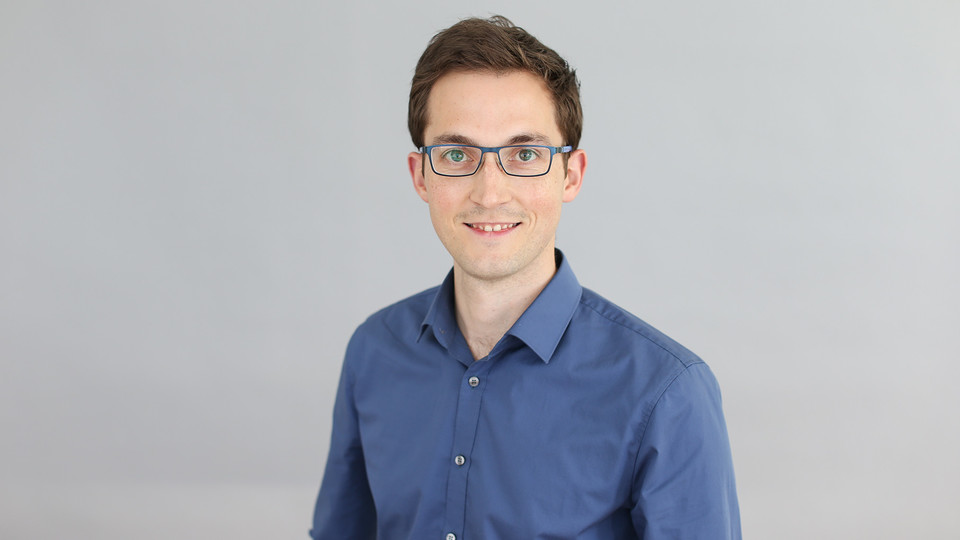 Portrait von Andreas Gerster. Er trägt ein blaues Hemd sowie eine Brille und lächelt.
