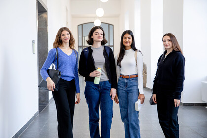 Vier junge Frauen stehen in einem weiß gestrichenen Flur des Mannheimer Schlosses. Sie schauen selbstbewusst in die Kamera.
