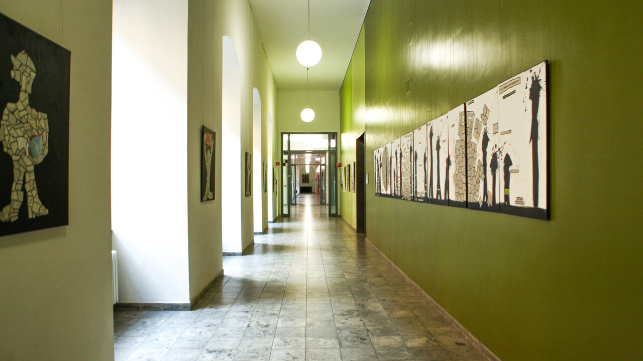 Ein Flur mit Bögen, welche an der linken Wand entlanglaufen, ist geschmückt mit Kunstwerken, die aus Zeitungscollagen und Farbklecks-Figuren bestehen.