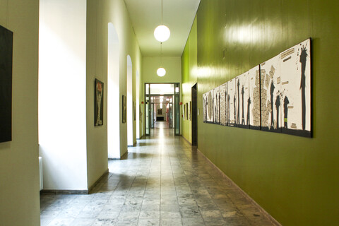 Ein Flur mit Bögen, welche an der linken Wand entlanglaufen, ist geschmückt mit Kunstwerken, die aus Zeitungscollagen und Farbklecks-Figuren bestehen.
