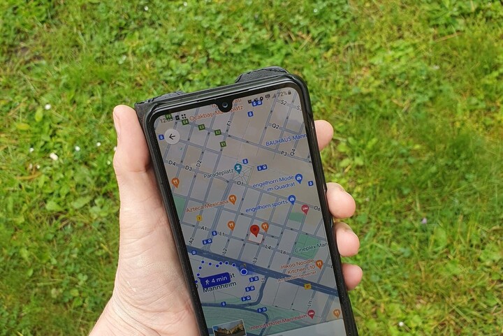 Eine Hand, die ein Smartphone hält, auf dem eine Navigationsapp offen ist. Der Bildschirm zeigt eine Karte.