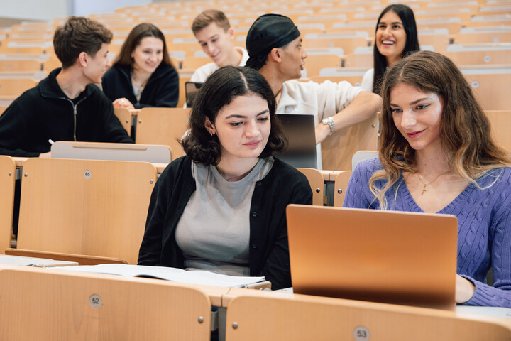 Junge Menschen sitzen im Vorlesungssaal. Einige haben Laptops vor sich.