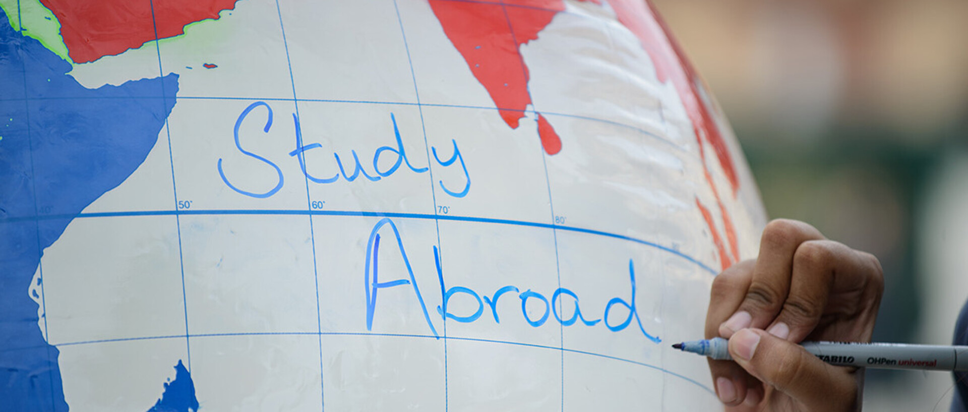 Eine Hand schreibt "Study Abroad" auf einen aufgeblasenen Globus
