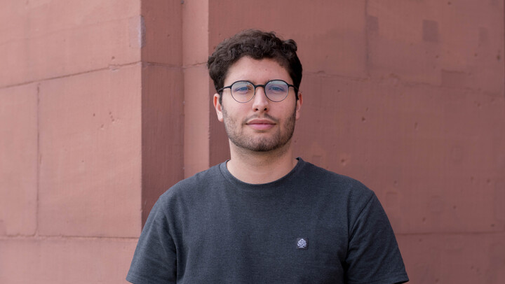 Adrià Mateu. He is wearing a black T-shirt and is standing in front of a brown wall.