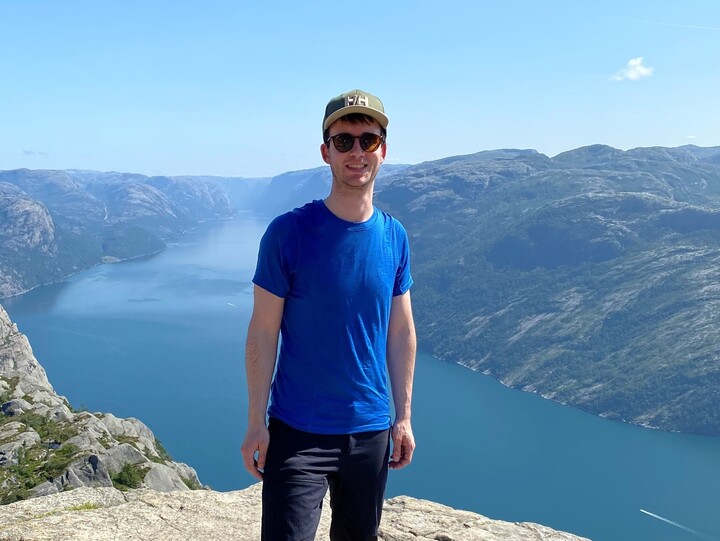 Eine Person in Wanderkleidung steht auf einem Felsvorsprung. Im Hintergrund ist ein See und Gebirge. Die Person heißt Timo Eberhard.