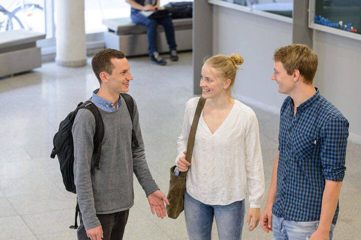 Drei Studierende stehen im Gebäude der Business School und unterhalten sich