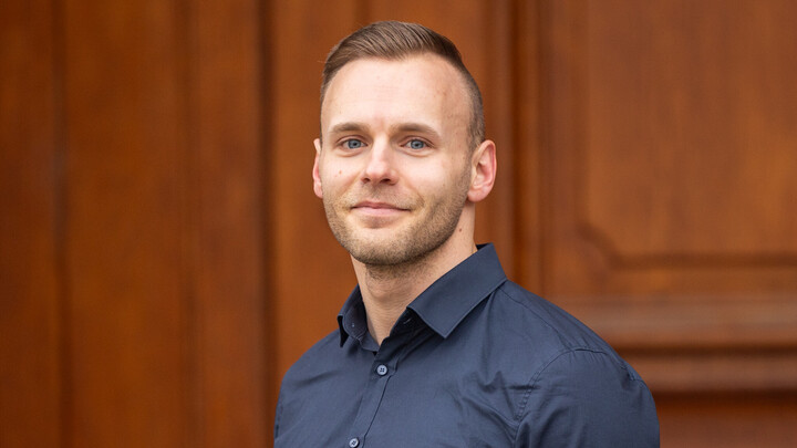 Portrait of Stefan Eschenwecker. He is wearing a black shirt and standing next to a building.
