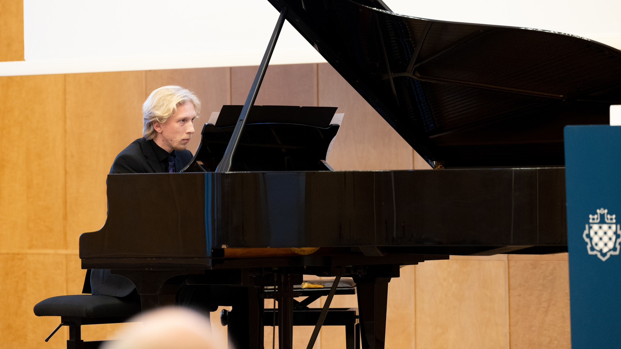 Ein Mann mit blonden Haaren spielt auf dem Flügel in der Aula der Uni Mannheim