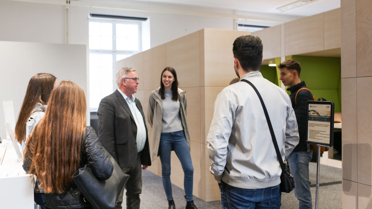 Eine Gruppe von Studierenden bei einer Führung vor dem Eingang des Learning Centers. Im Hintergrund modernes Mobiliar.