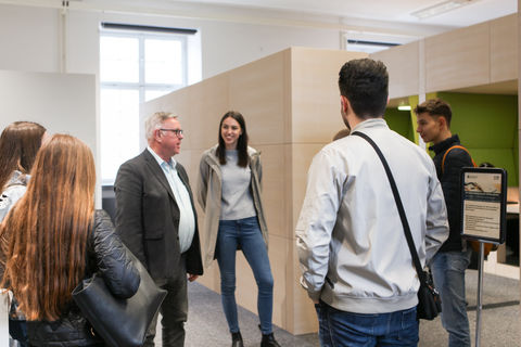 Eine Gruppe von Studierenden bei einer Führung vor dem Eingang des Learning Centers, einem hellen und modern möblierten Raum.
