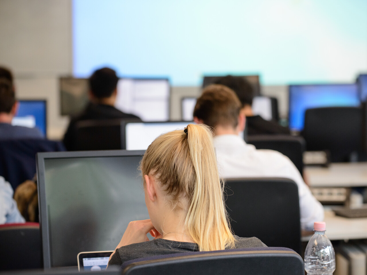 Computer Room Rückenansicht von Studierenden, die in Reihen an Computer-Bildschirmen sitzen.