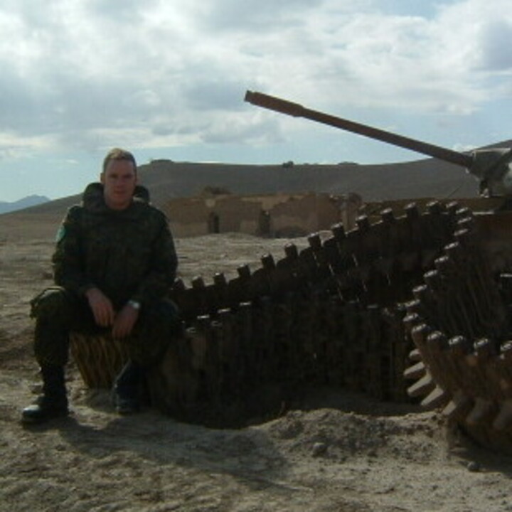 Ein Soldat sitzt an einem Panzer in einer kargen Landschaft
