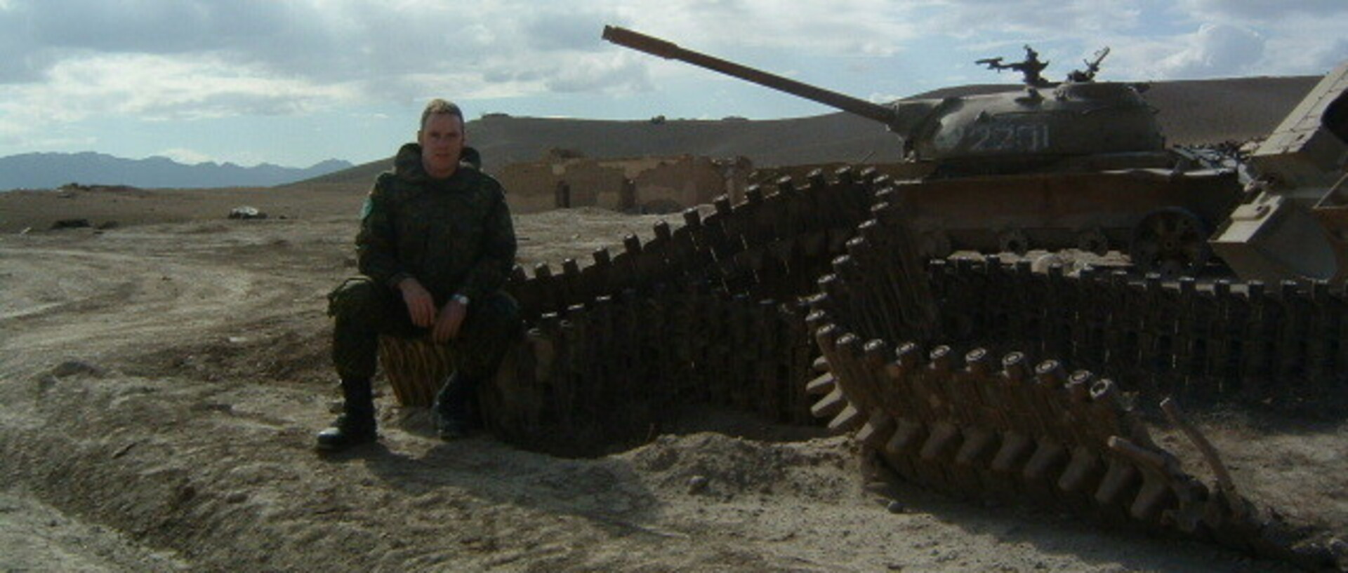 Ein Soldat sitzt an einem Panzer in einer kargen Landschaft
