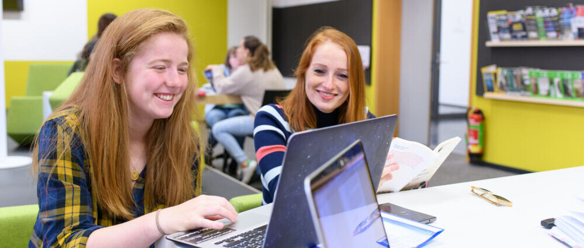 Zwei Studentinnen blicken lachend auf einen Laptop.