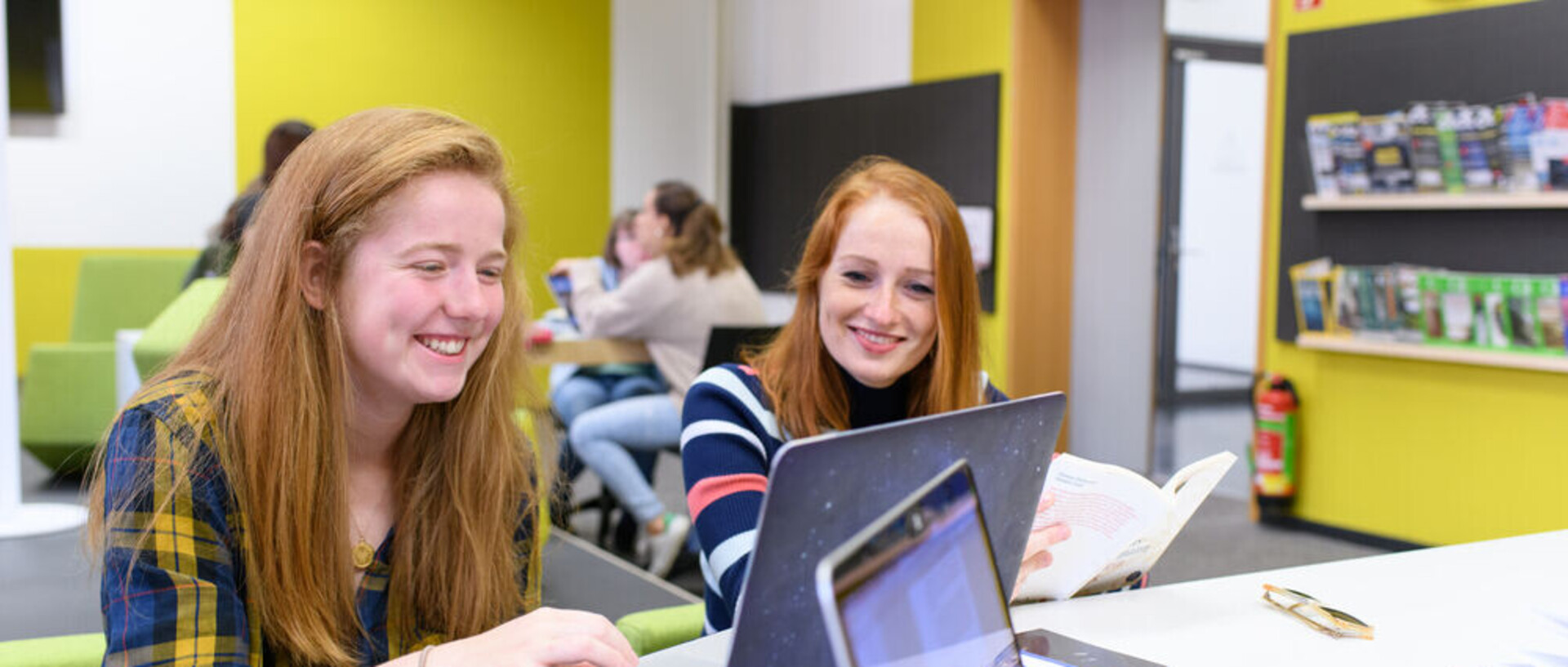 Zwei Studentinnen blicken lachend auf einen Laptop.