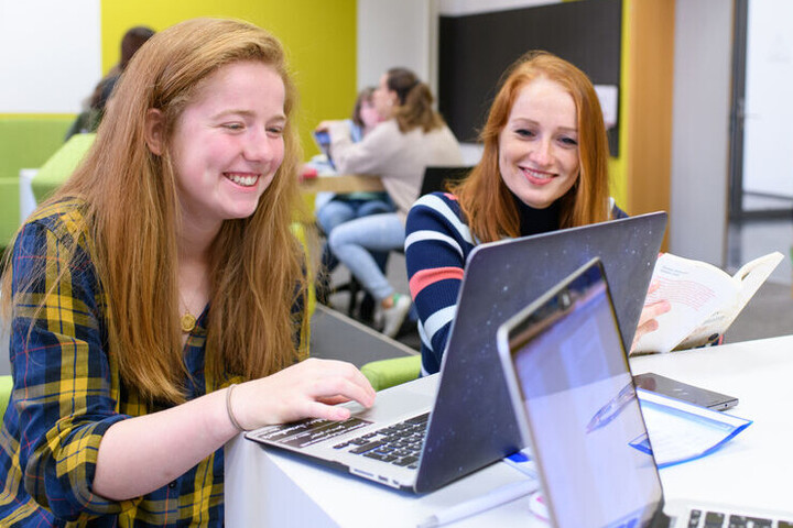 Zwei Studentinnen blicken lachend auf einen Laptop.