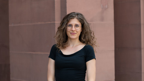 Elisabetta Girardi. She is wearing a black T-shirt and is standing in front of brown stonewall.