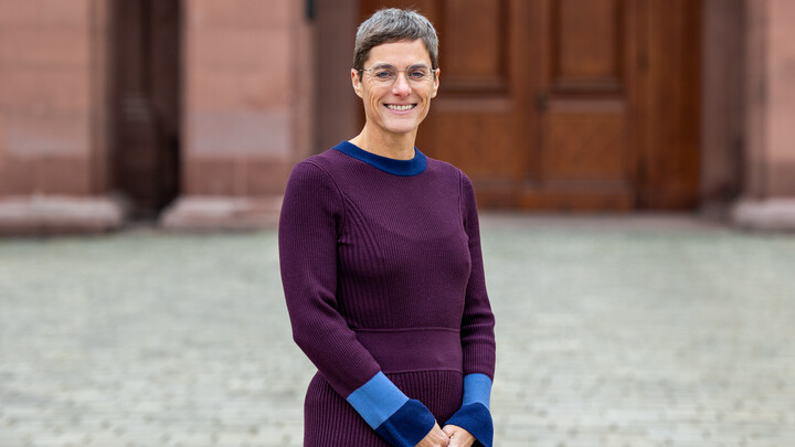 Portraitfoto von Prof. Dr. Tina In-Albon vor dem Schloss Mannheim. Sie trägt ein lila-blaues Kleid.