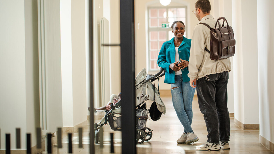 Zwei Personen mit Kinderwagen in einem Flur der Universität